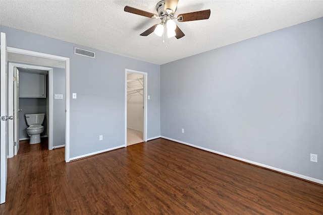 unfurnished bedroom featuring a textured ceiling, dark wood-type flooring, visible vents, baseboards, and a walk in closet