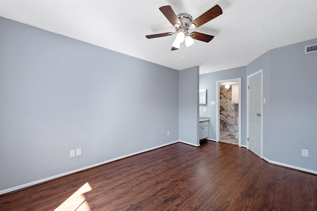 unfurnished bedroom featuring ensuite bath, baseboards, dark wood finished floors, and a textured ceiling