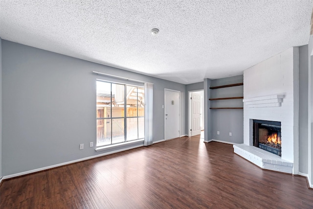 unfurnished living room featuring a brick fireplace, dark wood finished floors, a textured ceiling, and baseboards
