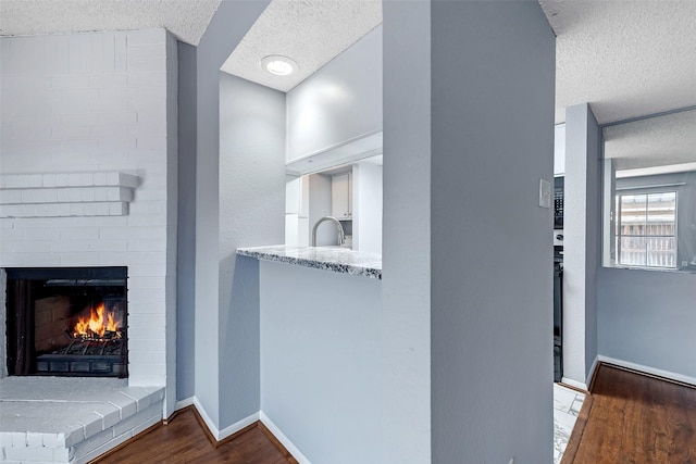 interior space featuring a textured ceiling, a brick fireplace, wood finished floors, and baseboards