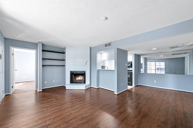 unfurnished living room with a textured ceiling, a brick fireplace, dark wood finished floors, and visible vents