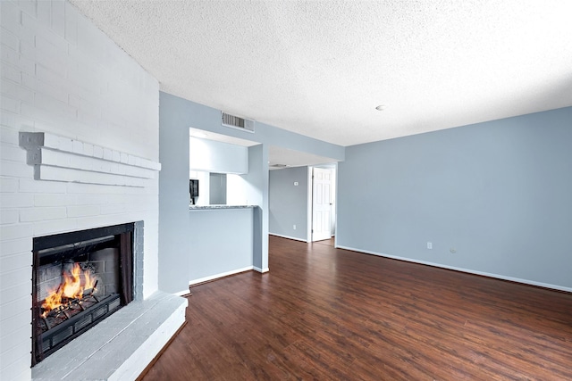 unfurnished living room featuring a textured ceiling, wood finished floors, visible vents, baseboards, and a brick fireplace