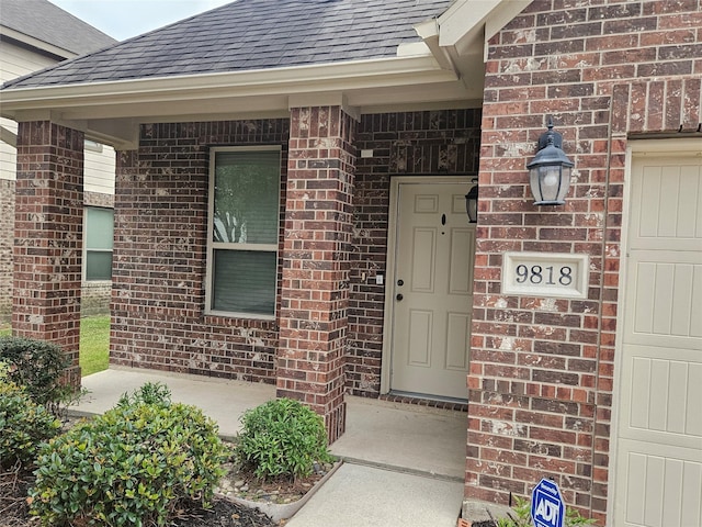 property entrance with a garage, brick siding, and roof with shingles