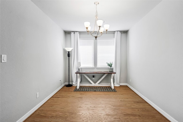 unfurnished dining area with baseboards, wood finished floors, and a notable chandelier