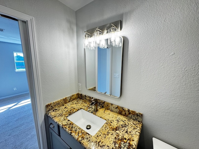 bathroom with toilet, a textured wall, vanity, and visible vents