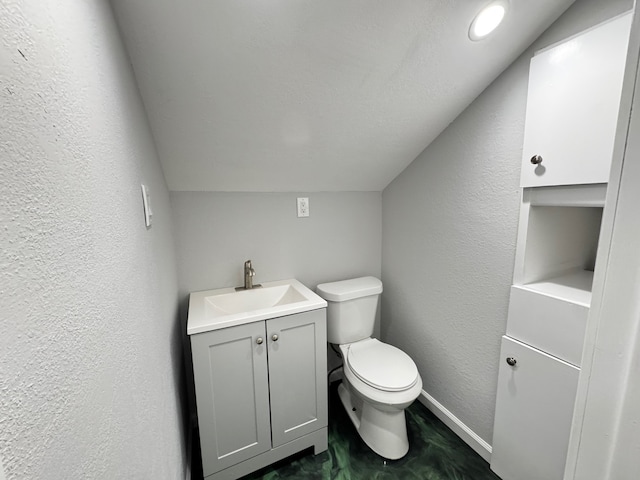 bathroom featuring a textured wall, toilet, vaulted ceiling, vanity, and baseboards