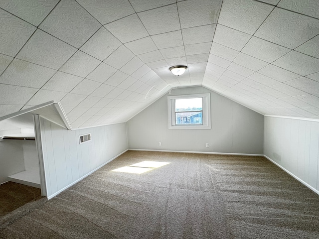 bonus room with lofted ceiling, wood walls, carpet, and visible vents