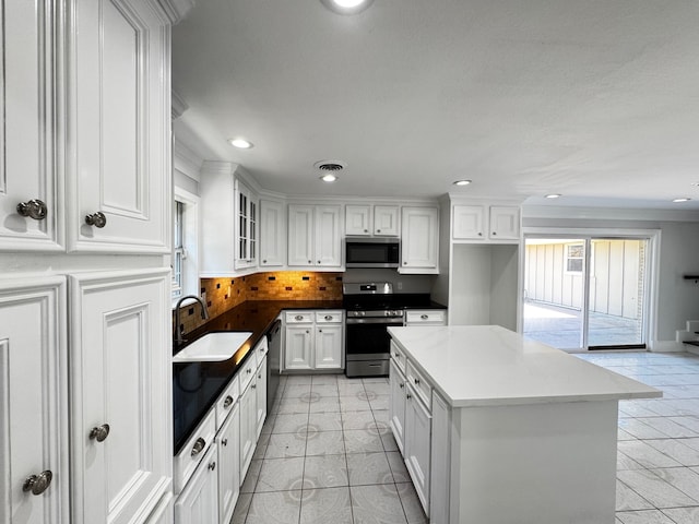 kitchen with appliances with stainless steel finishes, backsplash, a sink, and white cabinets