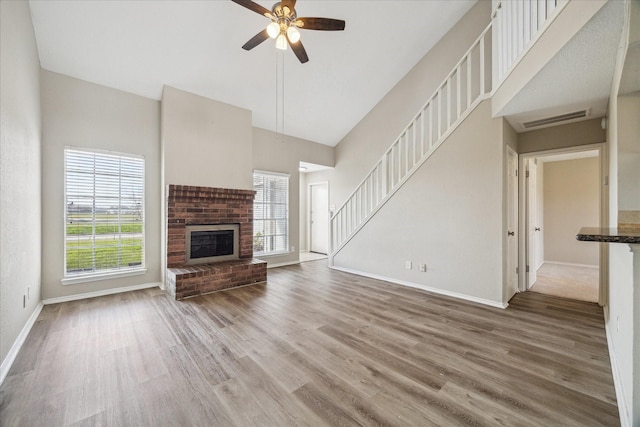 unfurnished living room with a brick fireplace, visible vents, stairway, and wood finished floors