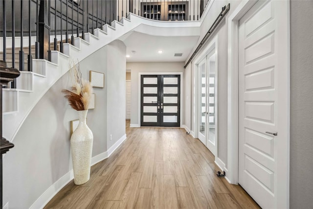 foyer featuring baseboards, wood finished floors, stairs, a high ceiling, and french doors