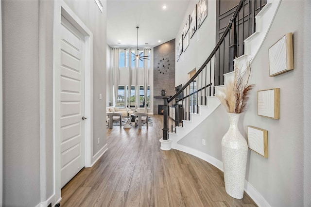 entryway featuring a towering ceiling, a large fireplace, ceiling fan, wood finished floors, and baseboards