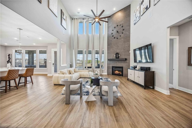 living room with light wood-type flooring, a tile fireplace, baseboards, and ceiling fan with notable chandelier