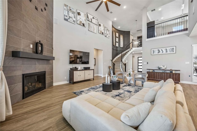 living area featuring stairs, a tiled fireplace, baseboards, and wood finished floors