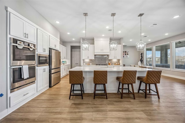 kitchen with light wood-style floors, white cabinetry, appliances with stainless steel finishes, and backsplash