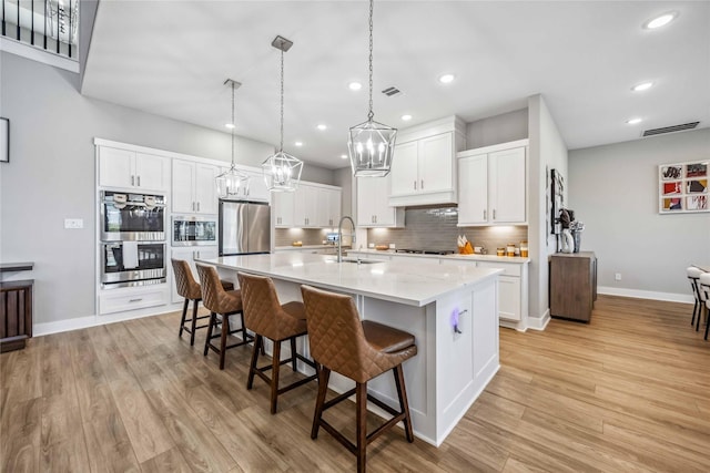 kitchen with light wood-style flooring, a sink, white cabinets, appliances with stainless steel finishes, and tasteful backsplash