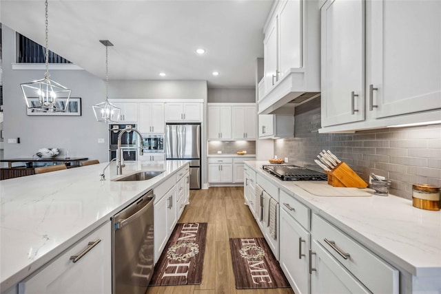 kitchen featuring white cabinets, decorative backsplash, light wood-style flooring, appliances with stainless steel finishes, and an inviting chandelier