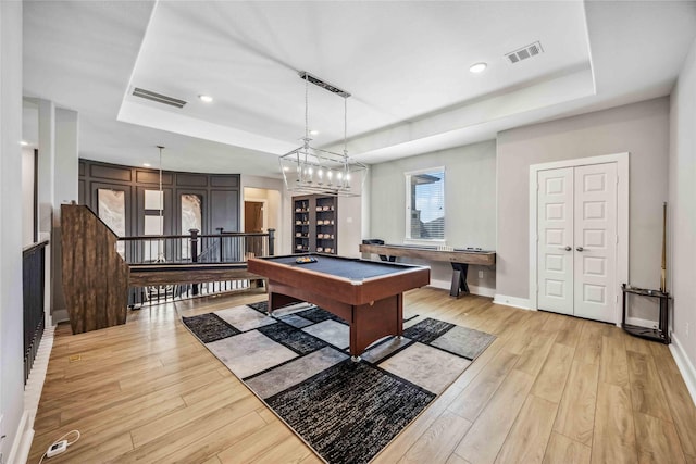 recreation room with a tray ceiling, light wood-type flooring, and visible vents