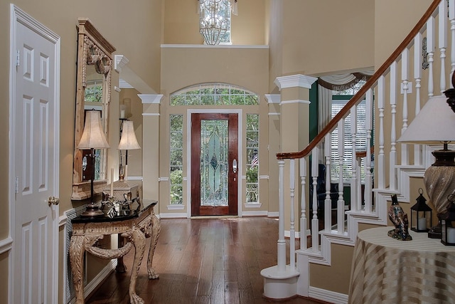 entryway featuring decorative columns, wood-type flooring, stairs, a high ceiling, and a notable chandelier