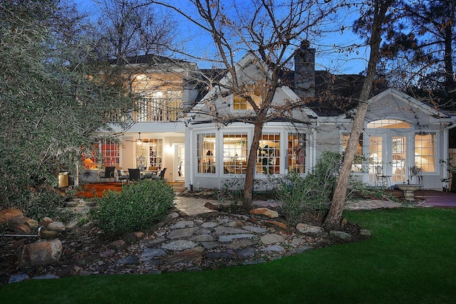 back of house with covered porch, a chimney, a lawn, and stucco siding