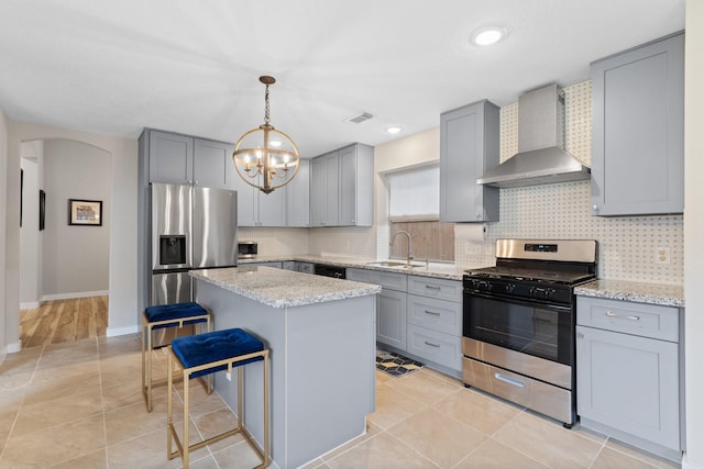 kitchen with wall chimney range hood, stainless steel appliances, a sink, and gray cabinetry