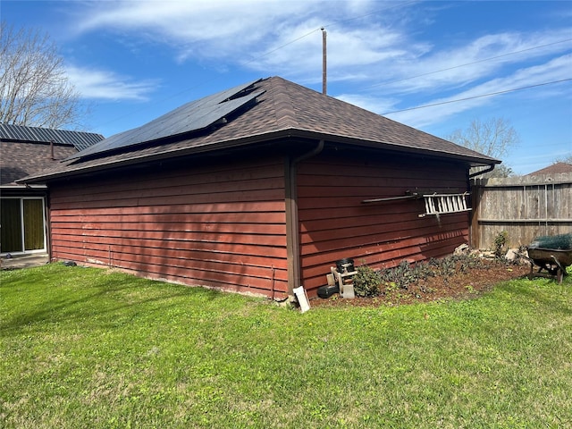 view of property exterior featuring a yard, a shingled roof, fence, and roof mounted solar panels