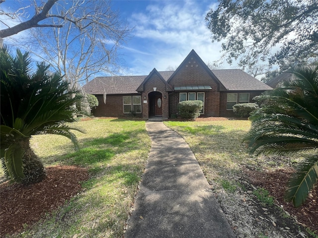 tudor-style house with a shingled roof, a front yard, and brick siding