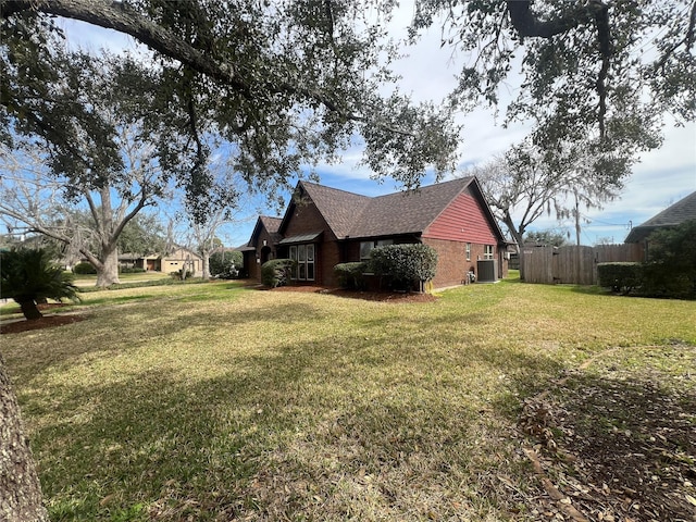 view of property exterior featuring cooling unit, brick siding, fence, roof with shingles, and a lawn