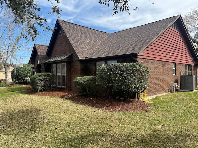 view of side of home with cooling unit, brick siding, a yard, and roof with shingles