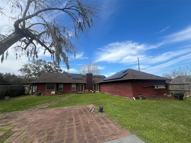 back of property with a yard, fence, and roof mounted solar panels