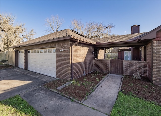 view of property exterior featuring concrete driveway, roof with shingles, an attached garage, fence, and brick siding