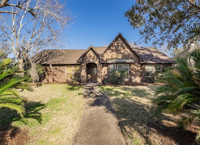 view of front of house featuring a front yard, brick siding, and roof with shingles