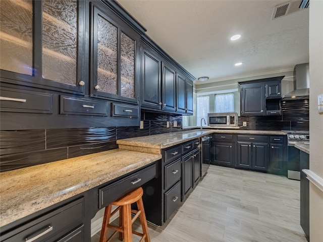 kitchen featuring visible vents, decorative backsplash, glass insert cabinets, appliances with stainless steel finishes, and wall chimney range hood