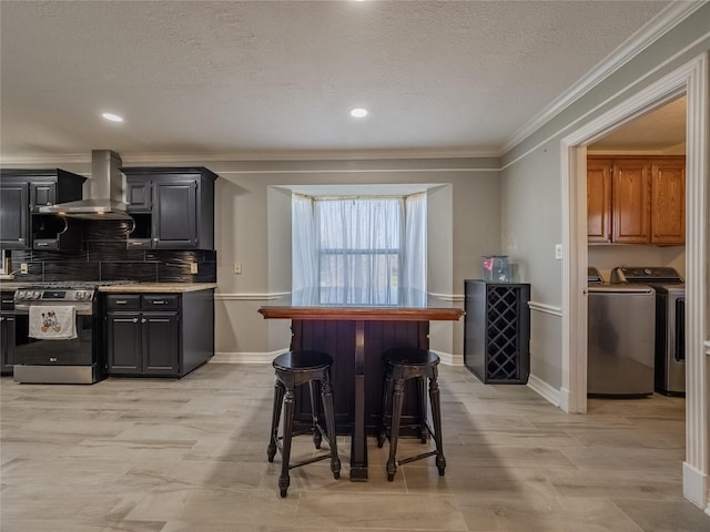 kitchen featuring crown molding, washing machine and clothes dryer, tasteful backsplash, wall chimney range hood, and gas range