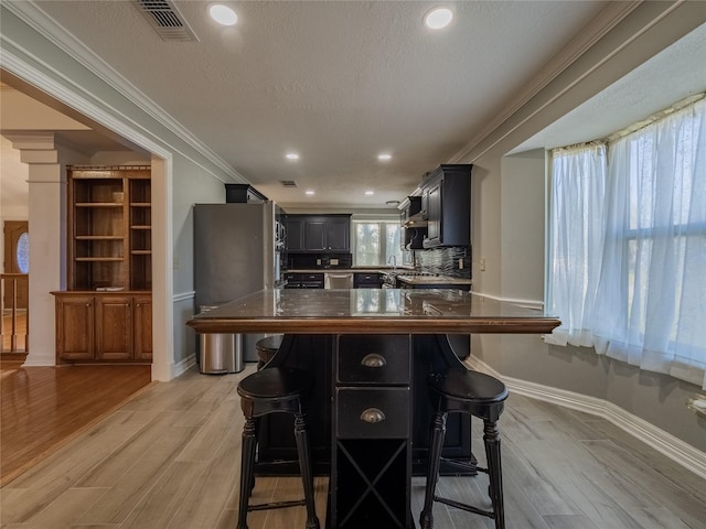 kitchen with a breakfast bar, freestanding refrigerator, a textured ceiling, crown molding, and light wood-type flooring