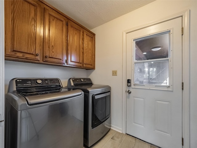 laundry room featuring a textured ceiling, light wood-style flooring, baseboards, cabinet space, and washing machine and clothes dryer