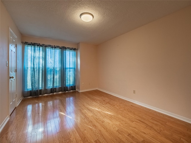 spare room with a textured ceiling, wood-type flooring, and baseboards