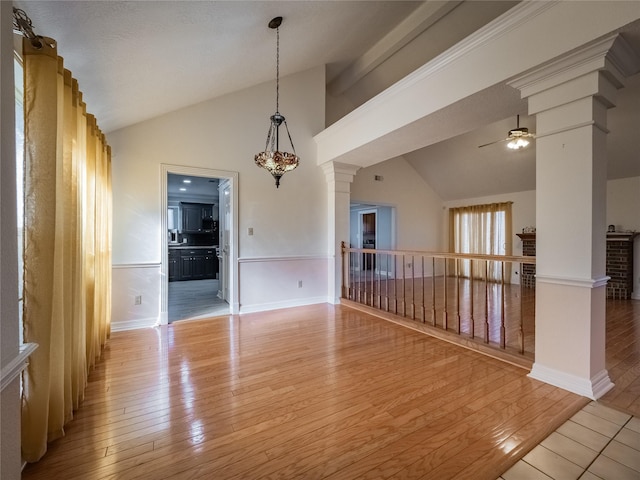 spare room featuring high vaulted ceiling, ceiling fan with notable chandelier, decorative columns, and hardwood / wood-style flooring