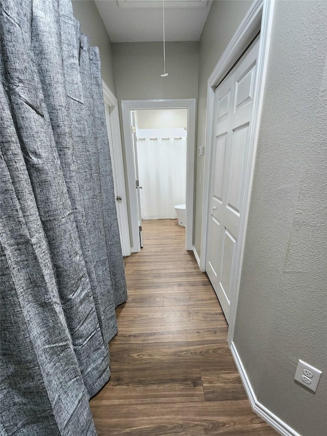 hallway featuring attic access, wood finished floors, baseboards, and a textured wall