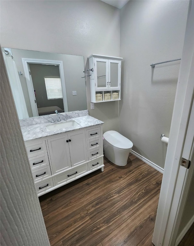 bathroom with vanity, toilet, wood finished floors, and baseboards