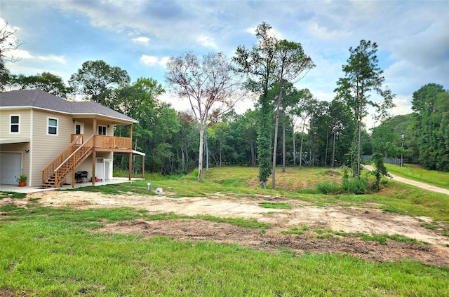 view of yard featuring driveway, a wooden deck, an attached garage, and stairs