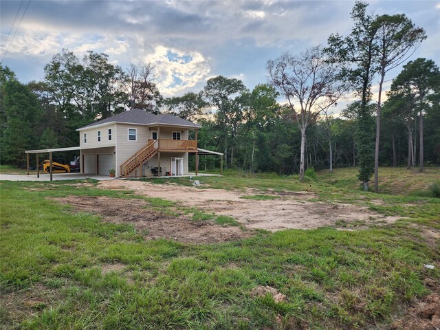 view of yard with a deck, an attached garage, stairs, and dirt driveway