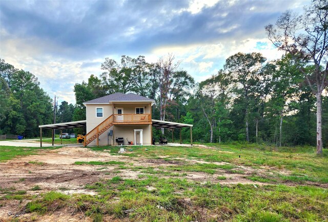rear view of property featuring stairway, an attached carport, a wooded view, and dirt driveway