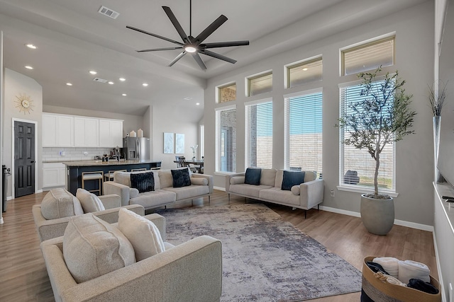 living area with light wood-style flooring, recessed lighting, a towering ceiling, visible vents, and baseboards