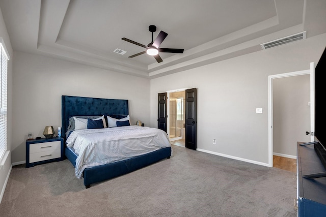 carpeted bedroom featuring ensuite bathroom, a ceiling fan, visible vents, baseboards, and a raised ceiling