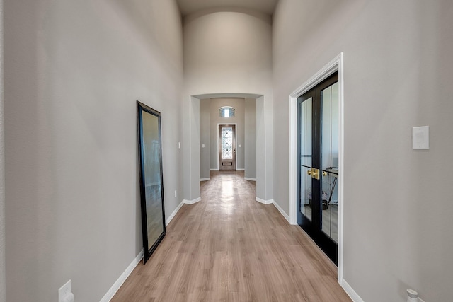 corridor with arched walkways, a high ceiling, baseboards, french doors, and light wood finished floors