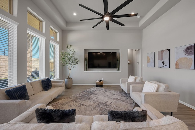 living area featuring recessed lighting, wood finished floors, a towering ceiling, a ceiling fan, and baseboards