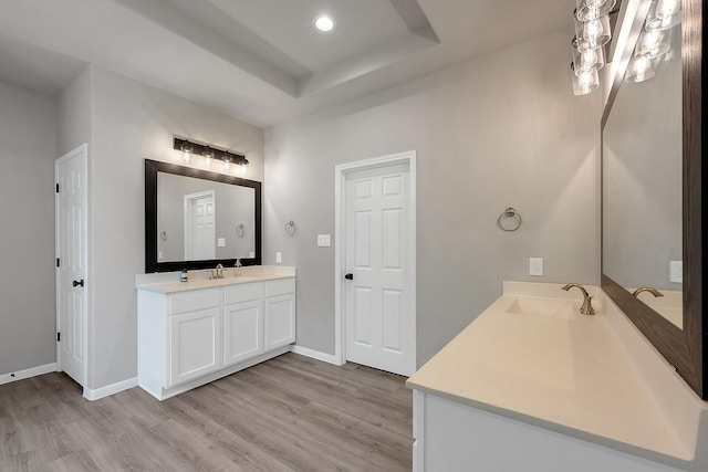 bathroom with recessed lighting, wood finished floors, vanity, baseboards, and a tray ceiling