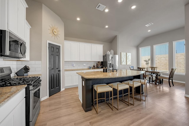 kitchen featuring visible vents, an island with sink, light wood-style flooring, appliances with stainless steel finishes, and a kitchen breakfast bar