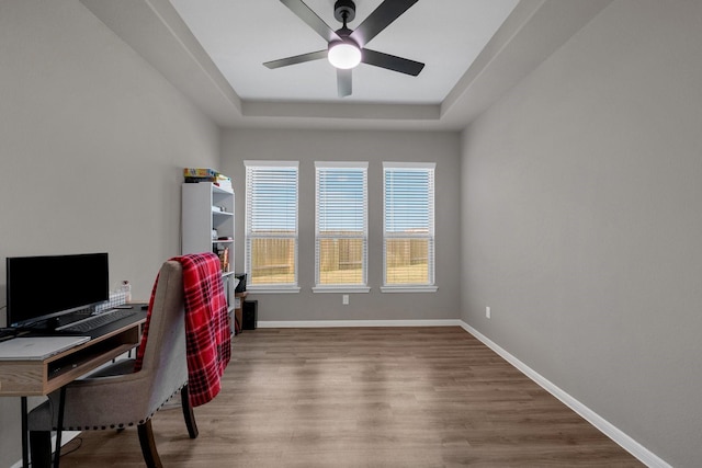 office featuring a tray ceiling, wood finished floors, a ceiling fan, and baseboards