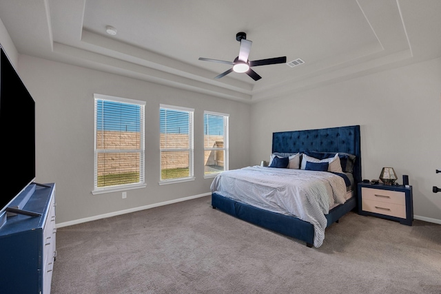 carpeted bedroom featuring ceiling fan, a tray ceiling, visible vents, and baseboards